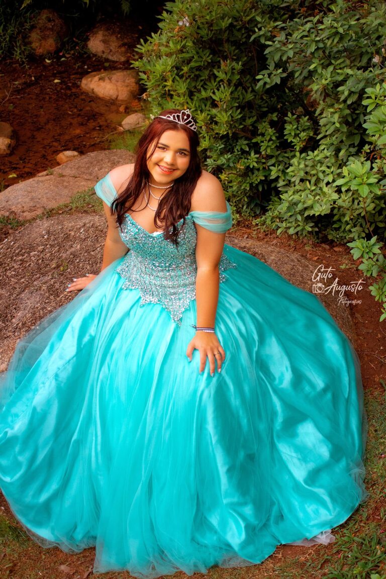 Alana em seu ensaio de 15 anos, vestida como uma princesa em um vestido azul deslumbrante, sentada em meio à natureza, capturada por Guto Augusto Fotografias