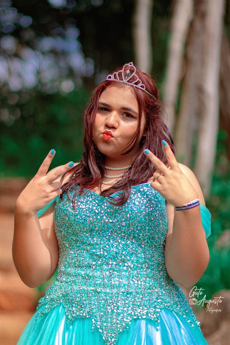 Alana fazendo uma pose divertida em seu ensaio de 15 anos, usando um vestido azul brilhante e tiara, capturada por Guto Augusto Fotografias.